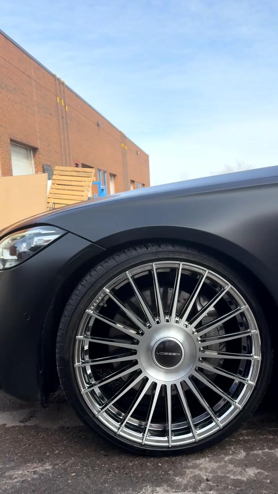 Polished multi-spoke chrome wheel on a satin black sedan at Cosmo Car Customs