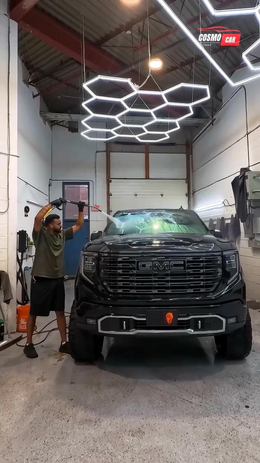 Cosmo Car Customs detailer pressure-washing a black GMC Sierra in the Mississauga studio