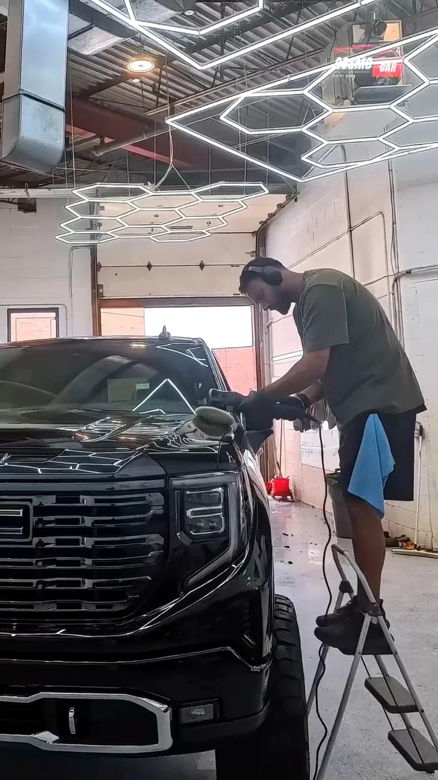 Technician working the front of a black GMC Sierra with a polisher in the studio