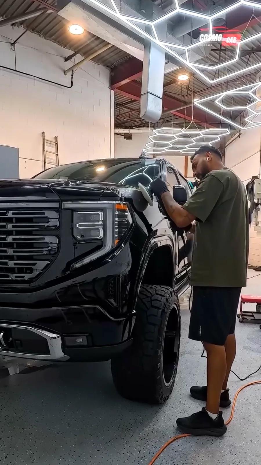 Cosmo Car Customs technician machine polishing the hood of a black GMC Sierra under the hex lights