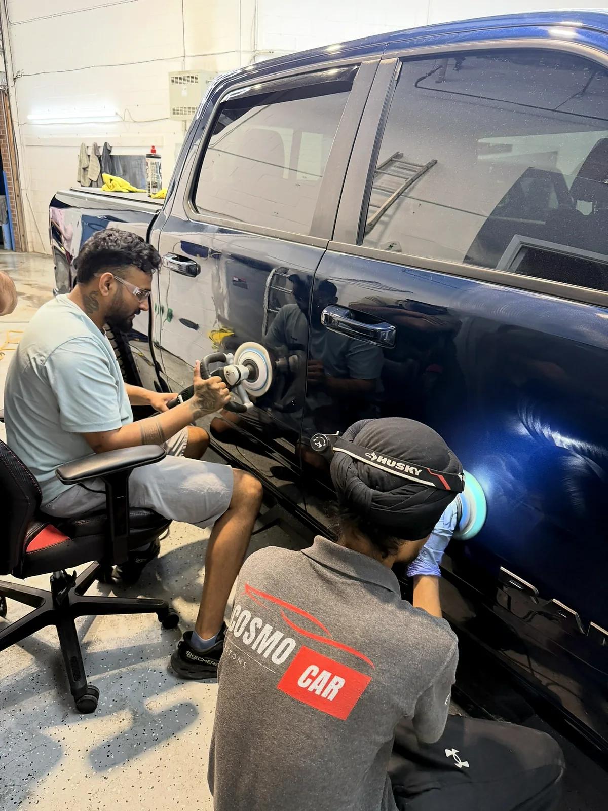 Two Cosmo Car Customs technicians correcting the doors of a black truck with machine polishers