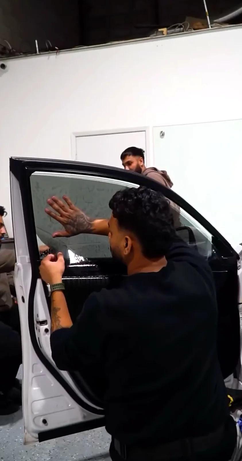 Cosmo Car Customs technician fitting window film to a car door in the studio
