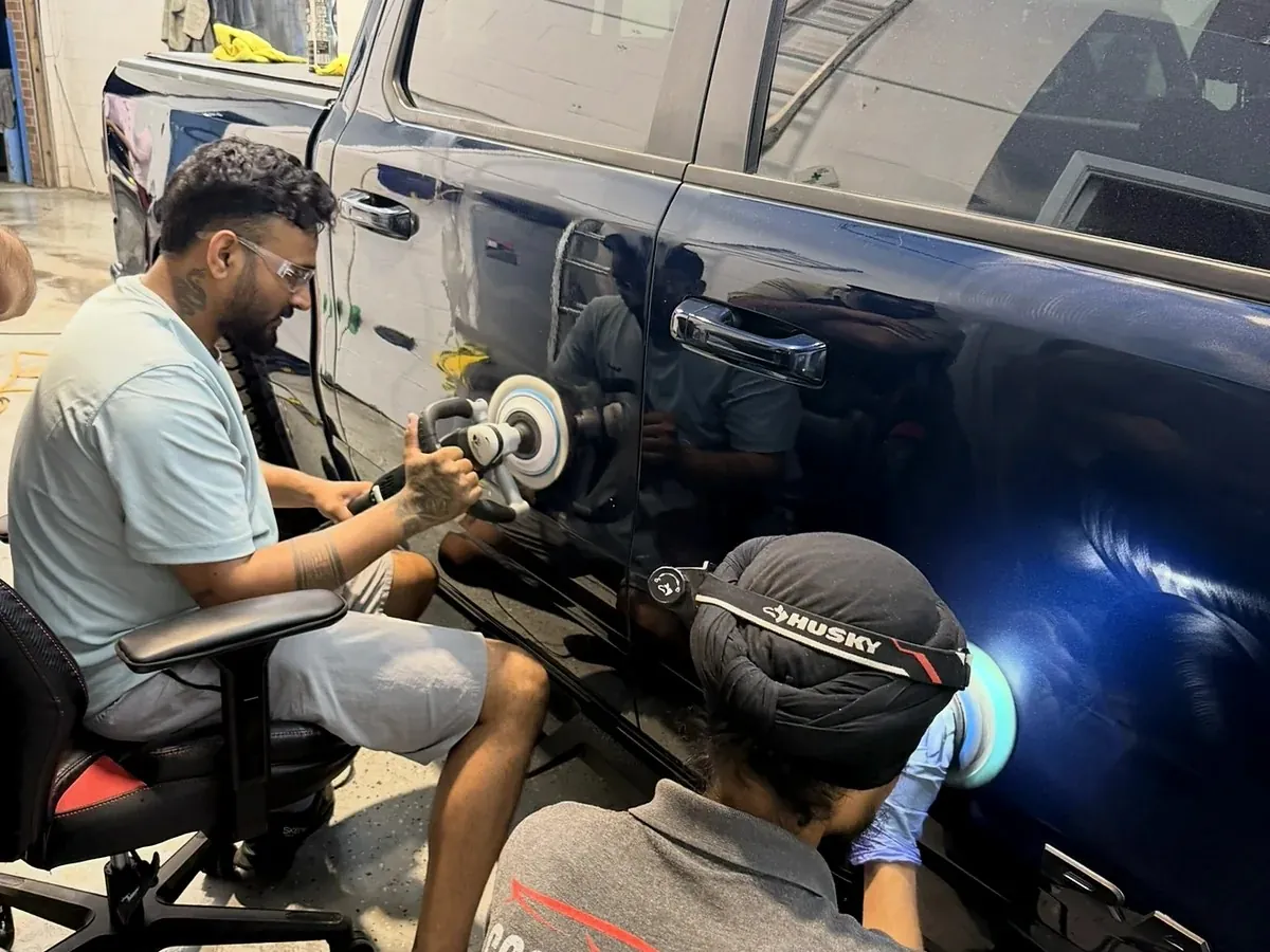 Two Cosmo Car Customs technicians correcting the doors of a dark blue truck with machine polishers