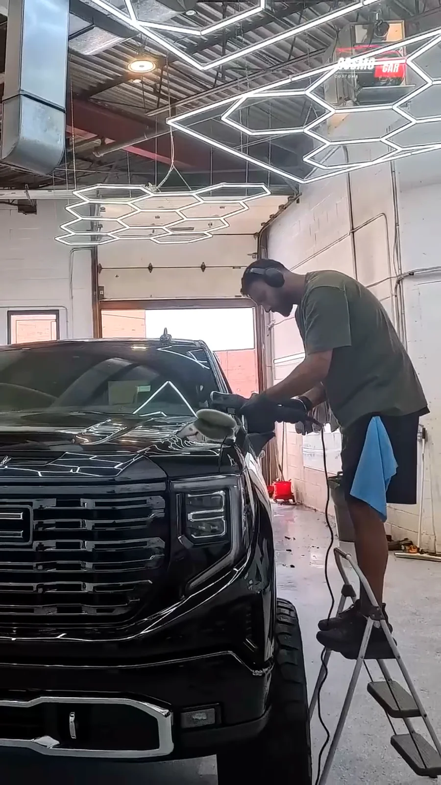 Technician working the front of a black GMC Sierra with a polisher in the studio