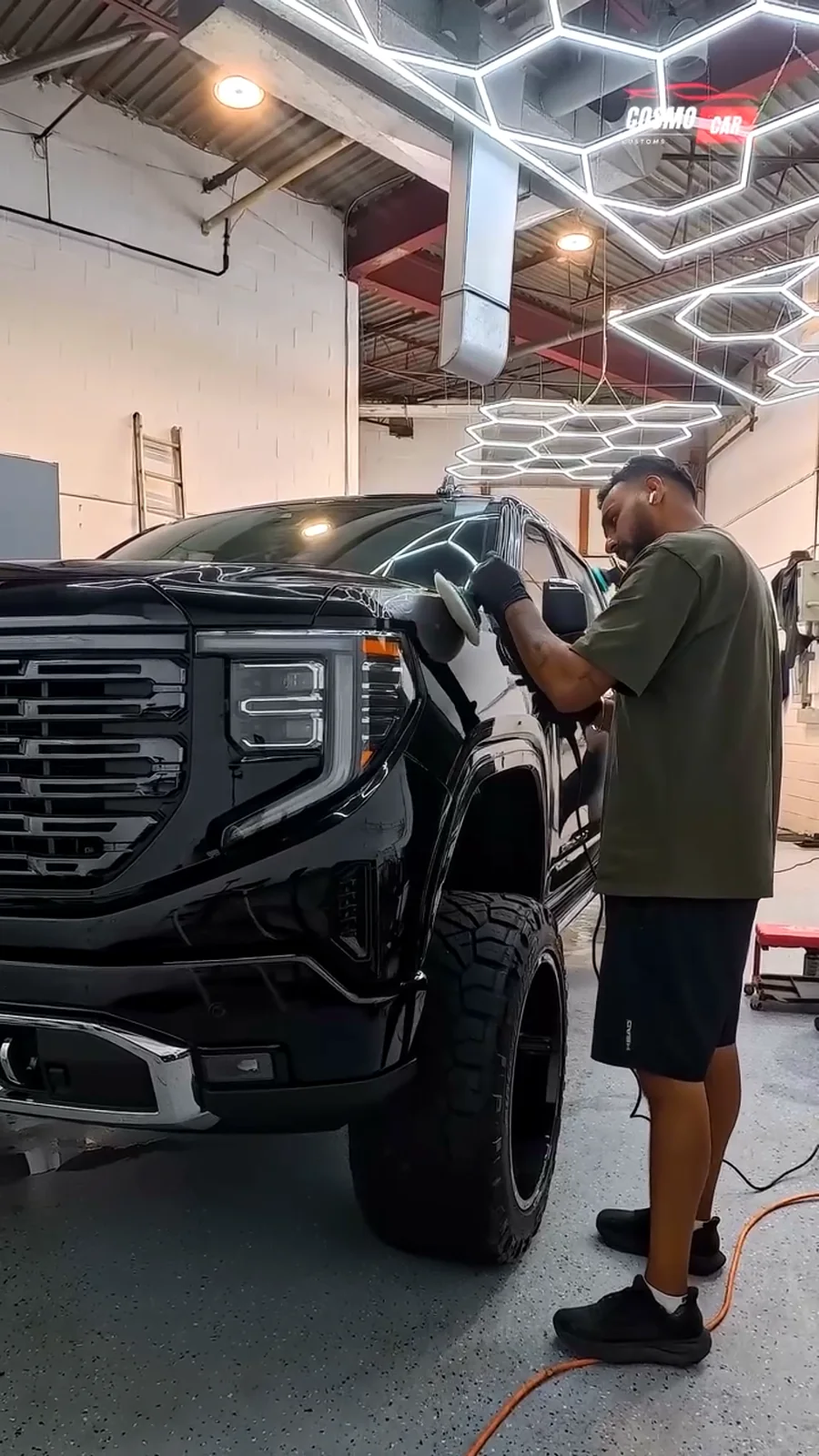 Cosmo Car Customs technician machine polishing the hood of a black GMC Sierra under the hex lights